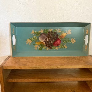 May include: Rectangular teal serving tray with a hand-painted fruit design. The tray features a cluster of grapes, a red apple, and other fruits and vegetables. It has white handles and gold accents.
