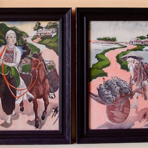 May include: Two framed Asian-themed prints. One depicts a woman with a basket and a horse. The other shows an elderly man pushing a cart with pigs. Both have black frames and are set against a light background.