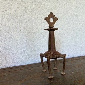 May include: A vintage, ornate metal candle holder with a dark brown finish. The candle holder has a tall, hexagonal stem supported by three legs. The top features a decorative, openwork design. The piece is likely made of cast iron.