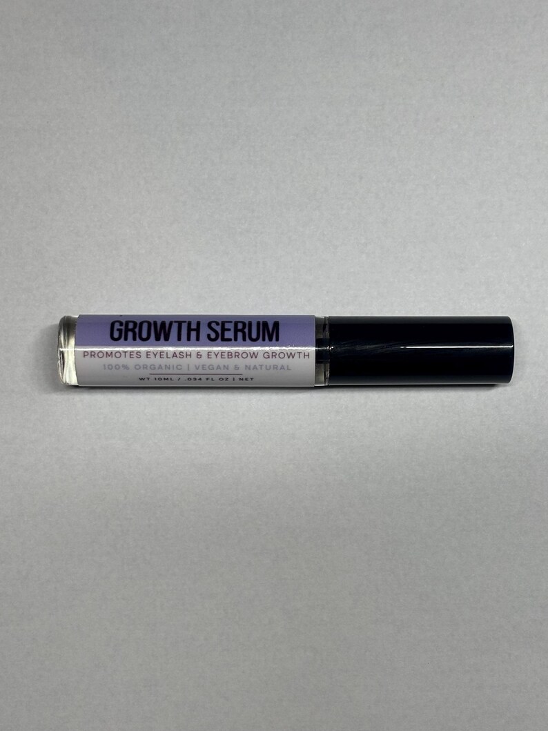Op de afbeelding: Een heldere glazen tube Growth Serum met een zwarte dop. Het label is lavendelkleurig met witte tekst met de tekst "Growth Serum" en "Promotes Eyelash & Eyebrow Growth". De tube is 24,6 ml.