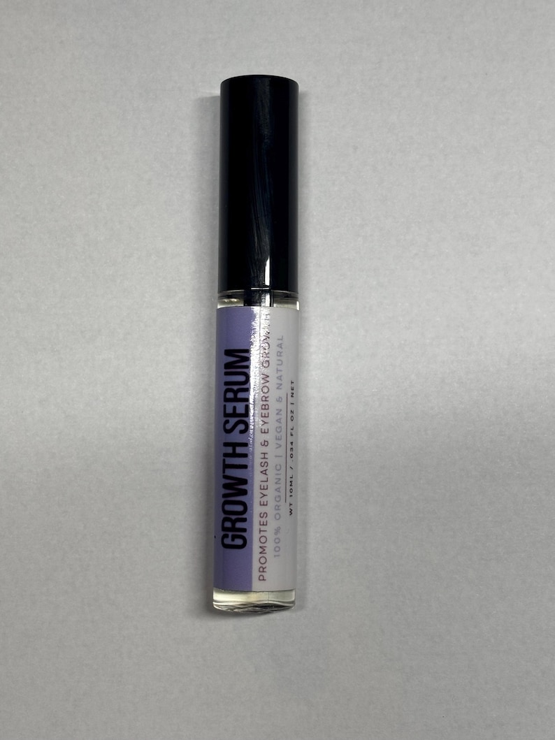 Op de afbeelding: Een cilindrische fles Growth Serum voor wimpers en wenkbrauwen. De fles heeft een zwarte dop en een heldere glazen body met een label met de tekst "GROWTH SERUM" en details over de biologische en veganistische samenstelling van het product.