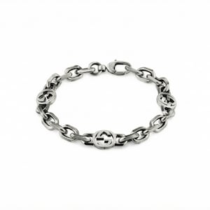 May include: Silver-toned chain bracelet with oval links and circular accents featuring a double-G logo. The bracelet is displayed on a white background, showcasing its polished metal finish and design.