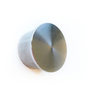 May include: A silver metal knob with a round, smooth, and shiny surface. The knob is attached to a wall.