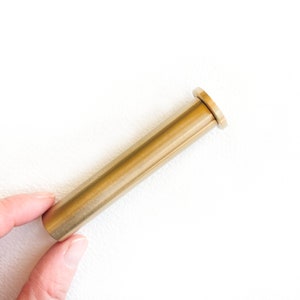 Może przedstawiać: Złoty metalowy pręt z zaokrąglonym końcem. Pręt ma około 15 cm długości.