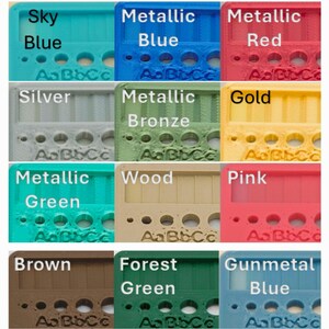K&ouml;nnte beinhalten: Eine Farbkarte mit einundzwanzig rechteckigen Kunststoffmustern, beschriftet mit Namen wie Royal Blue, Yellow, Red, Lavender, Lime Green, Orange, Sky Blue, Metallic Blue, Metallic Red, Silver, Metallic Bronze, Gold, Metallic Green, Wood, Pink, Brown, Forest Green, Gunmetal Blue, Bare Silver, V. Grey, White, Charcoal Grey, Midnight Blue und Black, jeweils mit kreisf&ouml;rmigen Ausstanzungen und gepr&auml;gtem AaBbCc-Text.