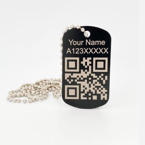 May include: Black dog tag with a silver ball chain. The tag features the text "Your Name" and "A123XXXXXX" above a QR code. The tag has a simple, modern design.