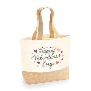 May include: A canvas tote bag with a natural beige base and handles. The bottom section is a light brown burlap material. The bag features the text "Happy Valentine's Day!" surrounded by pink and red hearts.