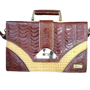 May include: A brown and tan leather handbag with a crocodile pattern. The bag has a gold-toned clasp and a shoulder strap.