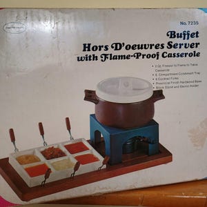 May include: A vintage buffet hors d'oeuvres server with a flame-proof casserole. The set includes a 6-compartment condiment tray, cocktail forks, and a black stand. The casserole is brown with a white lid.