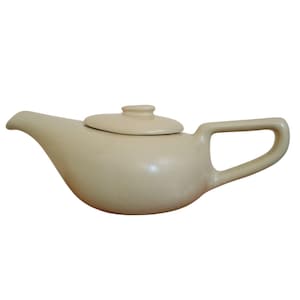 May include: A cream-colored ceramic teapot with a curved spout, a lid, and a rectangular handle. The teapot has a smooth, glossy finish and a classic design, suitable for serving tea. The teapot measures approximately 9 inches in length.