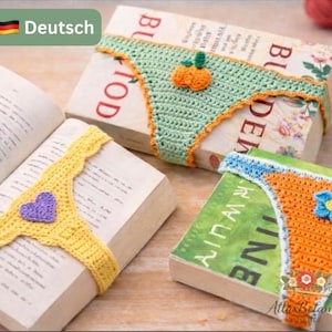 Può includere: Accessori per libri all'uncinetto a forma di biancheria intima. Uno è giallo con un cuore viola, un altro è verde con una zucca arancione e il terzo è arancione con un fiore blu. Sono posizionati sopra i libri.