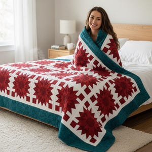 May include: A red and white quilt with a floral pattern, framed by a teal border, is draped over a bed. The quilt features a repeating design of red flowers set against a white background. The quilt is made of soft material.