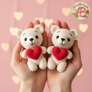 Peut inclure: Deux oursons en crochet blanc cassé, chacun tenant un cœur rouge. Les oursons ont des yeux noirs et des visages souriants. Le fond est rose clair avec des lumières bokeh en forme de cœur. Les oursons sont tenus dans des mains ouvertes.