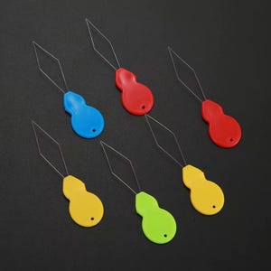 May include: A collection of colorful plastic loop turners in red, blue, yellow, and green. Each tool has a teardrop-shaped handle and a thin, diamond-shaped wire loop. The tools are arranged on a dark surface.