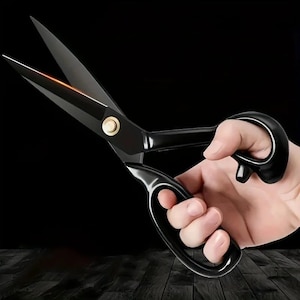 May include: A pair of black metal scissors with a gold-toned center screw. The blades are sharp and pointed, and the handles are designed with a large loop for the fingers and a smaller loop for the thumb, featuring a smooth, glossy finish.