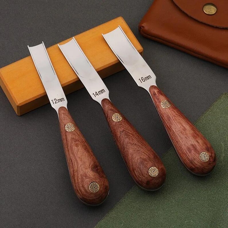 May include: Three leather craft edge bevelers with polished metal blades and wooden handles. The blades are marked 12mm, 14mm, and 16mm. Each handle features two decorative brass rivets with a circular pattern. The tools are arranged side by side.