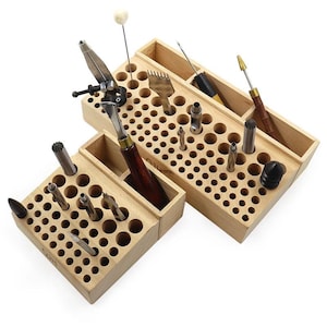 May include: Two light-colored wooden organizers with numerous circular holes of varying sizes for holding tools. The organizers contain various metal crafting implements, including punches, awls, and pliers with wooden and black handles.