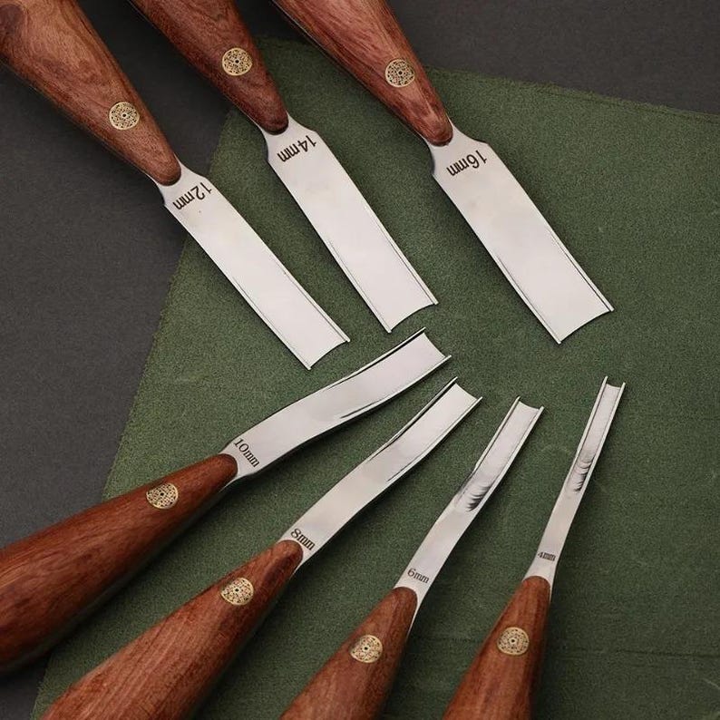May include: A set of seven woodworking gouges with polished metal blades and dark brown wooden handles. Each blade is stamped with its specific width, ranging from 4mm to 16mm, and features a small circular gold-toned metal inlay on the handle.