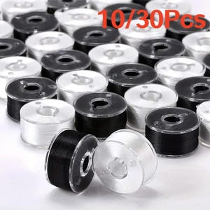 May include: A collection of sewing machine bobbins with clear plastic sides, wound with either black or white thread. The text 10/30Pcs is printed in red at the top. These cylindrical bobbins are arranged in a group, showing the thread colours.