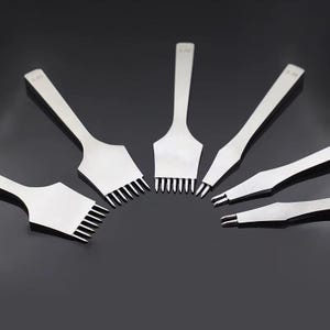 May include: A collection of silver leathercraft tools, including various sizes of stitching chisels and a pointed awl. The tools are arranged in a semi-circular pattern against a dark background, showcasing their sharp, precise edges.