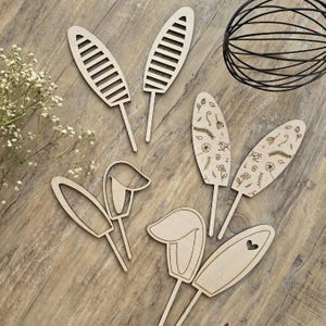 May include: A set of eight wooden cake toppers featuring various designs, including floral patterns, stripes, and abstract shapes. The toppers are made of natural wood and have a rustic, handmade aesthetic.