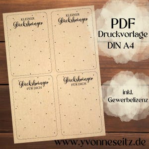 Könnte beinhalten: Ein Bogen Kraftpapier mit vier rechteckigen Etiketten, jeweils mit den Wörtern "Kleiner Glücksbringer" und "Für Dich" in eleganter Schrift. Der Bogen enthält auch den Text "PDF Druckvorlage DIN A4" und "inkl. Gewerbelizenz".