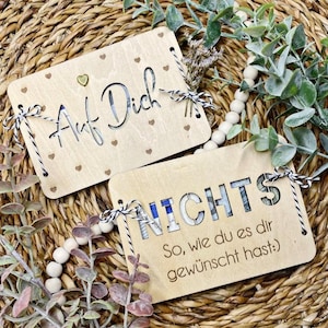 May include: Two wooden signs with a rustic look. The first sign says "Auf Dich" with small hearts in the background. The second sign says "Nichts So, wie du es dir gew&uuml;nscht hast."