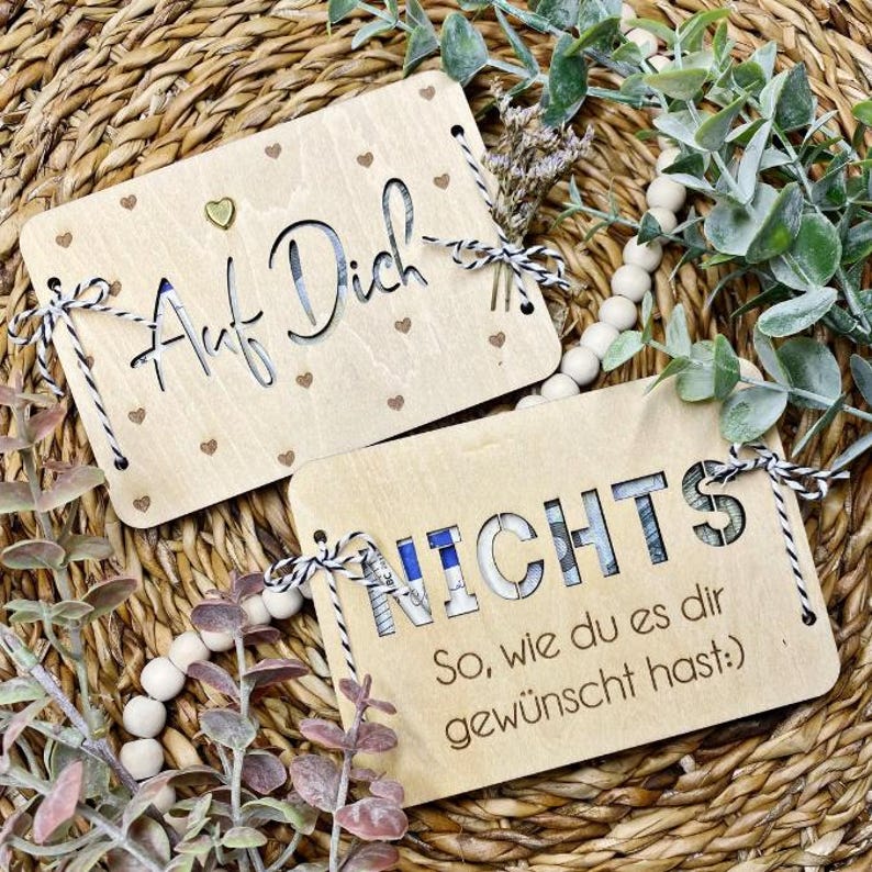May include: Two wooden signs with a rustic look. The first sign says "Auf Dich" with small hearts in the background. The second sign says "Nichts So, wie du es dir gew&uuml;nscht hast."