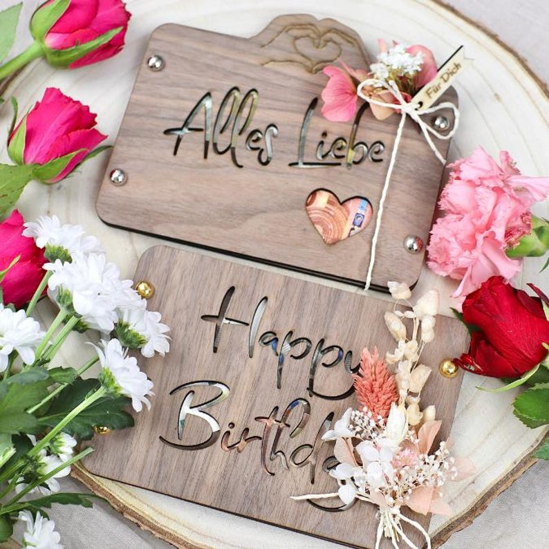 May include: Two wooden boxes with cut-out designs. The top box has the text "Alles Liebe" and a heart-shaped cutout. The bottom box has the text "Happy Birthday". Both boxes are decorated with dried flowers.