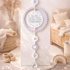 May include: A decorative wall hanging with a lavender scalloped edge and the text "Danke für die vielen unvergesslichen Erinnerungen". The hanging includes wooden beads, floral and heart shapes, and a crystal pendant. The color scheme is white and lavender.