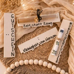Könnte beinhalten: Drei weiße rechteckige Holzschilder mit schwarzer Schrift. Eines zeigt GUTSCHEIN, eines Zeit, statt Zeug mit einem Glasröhrchen und eines Kleinigkeit von Herzen sowie WUNSCHERFÜLLER mit einem gerollten Geldschein mit 10 und 20 Aufdruck.