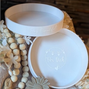 以下が含まれることがあります： 丸いベースと縁が盛り上がった2段の白いサービングトレイ。上段には「Hey Beautiful!」の文字、下段にはハート型のデザインの中に「Für Dich」の文字が書かれています。