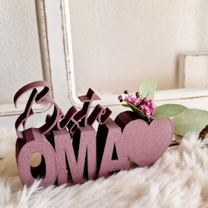 May include: A pink wooden sign that says "Beste Oma" with a small heart and a sprig of pink flowers.