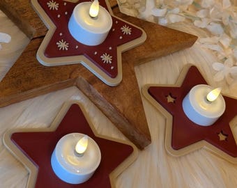 Puede incluir: Portavelas de madera en forma de estrella con un diseño de estrella roja y velas blancas que funcionan con pilas. Los portavelas en forma de estrella tienen un borde beige claro y están decorados con pequeños patrones de estrellas blancas. Las velas tienen una luz cálida y parpadeante.