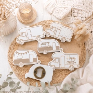 Könnte beinhalten: Eine Sammlung aus fünf weißen und beigen Holzornamenten in Wohnmobilform sowie einem Flaschenöffner. Zwei Wohnmobile tragen die Aufschriften Camping Glück und Happy Camper mit einem Herzsymbol. Die Designs zeigen verschiedene Wohnmobile.