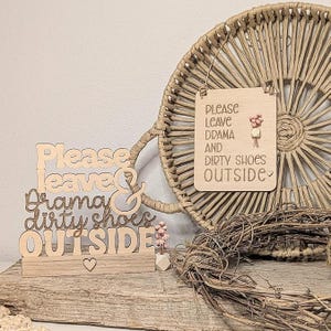 May include: Wooden sign with the text "Please Leave Drama and Dirty Shoes Outside" in a decorative font. The sign is light brown and has a heart symbol. A second sign with the same text hangs from a woven basket.