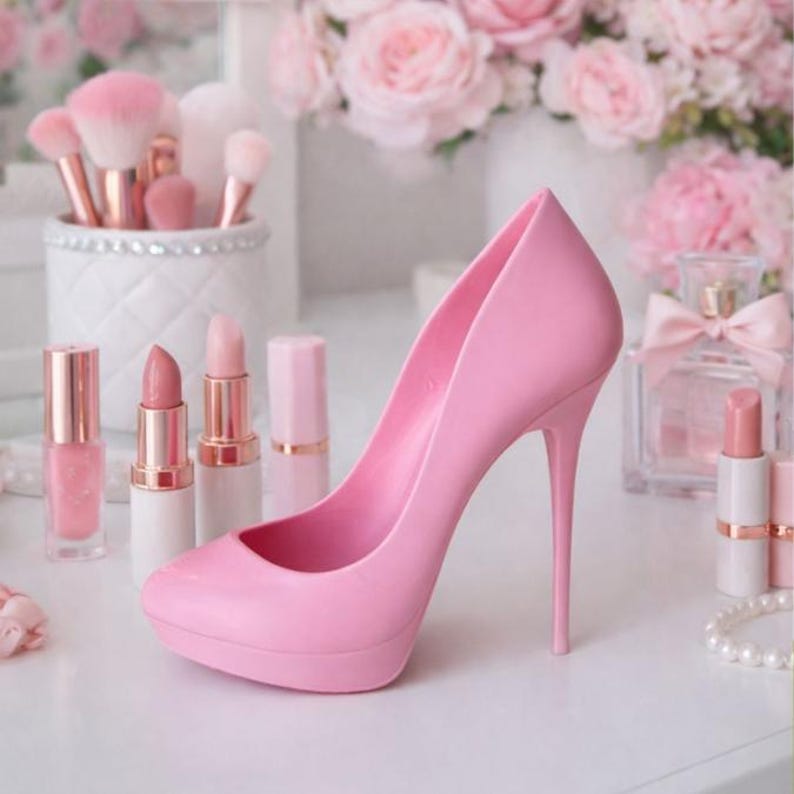 May include: A light pink high-heeled shoe is the focal point of this image, surrounded by beauty products. The stiletto heel and platform sole are visible. Lipsticks, makeup brushes, and perfume bottles in shades of pink complete the scene.