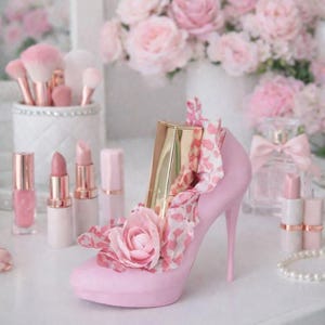 May include: A pink high-heeled shoe decorated with a pink flower and a gold lipstick tube. The shoe is surrounded by pink lipsticks, makeup brushes, and a perfume bottle, all in a soft, feminine aesthetic.