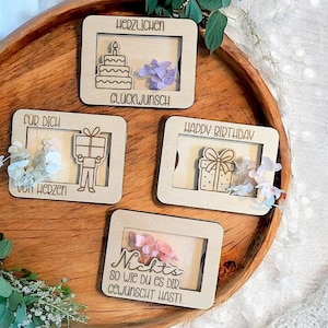 May include: Four wooden gift tags with laser-cut designs and text. One says "Happy Birthday" with a gift illustration. Another says "Für Dich von Herzen" with a person holding a gift. The other two say "Herzlichen Glückwunsch" and "Nichts so wie du es dir gewünscht hasti".
