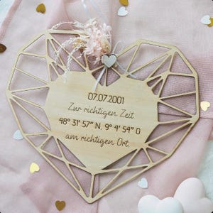 Könnte beinhalten: Holzherzförmige Plakette mit geometrischem Design und zentralem Bereich für Text. Die Plakette ist mit Trockenblumen und einem kleinen Herz verziert. Der Text enthält ein Datum, eine Uhrzeit und Koordinaten.
