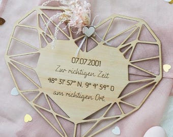 May include: A wooden heart-shaped plaque with a geometric design and a central area for text. The plaque is adorned with dried flowers and a small heart. The text includes a date, time, and coordinates.