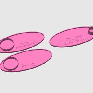 May include: Three pink oval-shaped coasters with a small circular indentation. The coasters have different phrases printed on them: "Du bist ph&auml;nomenal!" , "Smile", and "Gl&uuml;cklich steht dir gut!"