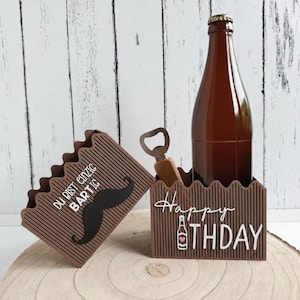 以下が含まれることがあります： 「Happy Birthday」の文字とビールのボトルのグラフィックが入った、茶色のビール瓶が入った装飾的なホルダー。別のホルダーには口ひげのグラフィックと「Du bist einzigartig Bartig」の文字が入っています。アンティークの栓抜きも含まれています。