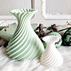 Puede incluir: Dos jarrones decorativos con un diseño en espiral. El jarrón más grande es verde claro y el jarrón más pequeño es blanco.