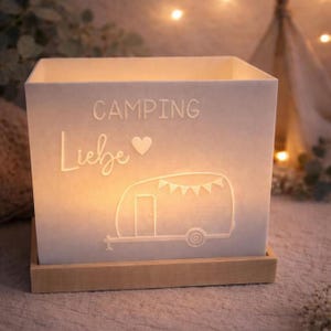Könnte beinhalten: Ein beleuchteter, quadratischer, weißer Papierlaterne mit den Worten "CAMPING Liebe" und einer Wohnwagen-Illustration. Die Laterne steht auf einem rechteckigen Holzsockel.