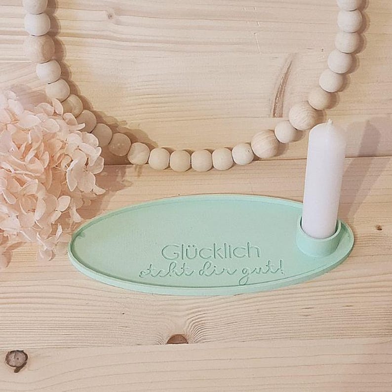 May include: A light green oval-shaped candle holder with a white candle and the text "Gl&uuml;cklich sieht dir gut!"