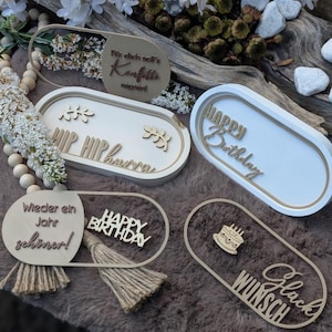 Pode incluir: Uma coleção de placas decorativas de madeira com várias frases, incluindo "Happy Birthday" e "Hip Hip Hurray". As placas apresentam uma paleta de cores neutras e são projetadas com uma estética moderna. Algumas placas têm um fundo branco.