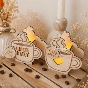 Könnte beinhalten: Zwei hellfarbene Kaffeetassen-Dekorationen aus Holz mit warmem Innenlicht. Eine Tasse trägt den Text "KAFFEE DATE?" und ein kleines Schild mit "FÜR DICH". Die andere Tasse zeigt einen herzförmigen Ausschnitt und ein Schild mit "Käffchen".