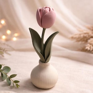May include: A handcrafted ceramic tulip sculpture. The sculpture features a light pink tulip bloom, green leaves, and a white vase. The tulip is a detailed, realistic representation of the flower, perfect for home decor.