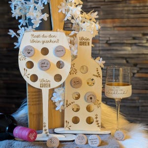Op de afbeelding: Houten wijnkurkdisplay in de vorm van een wijnglas en een fles. Het wijnglas heeft de tekst "Hast du den Wein gesehen?" en "Wein Korken". De fles heeft de tekst "Wein Korken". Decoratieve wijnkurken zijn inbegrepen.